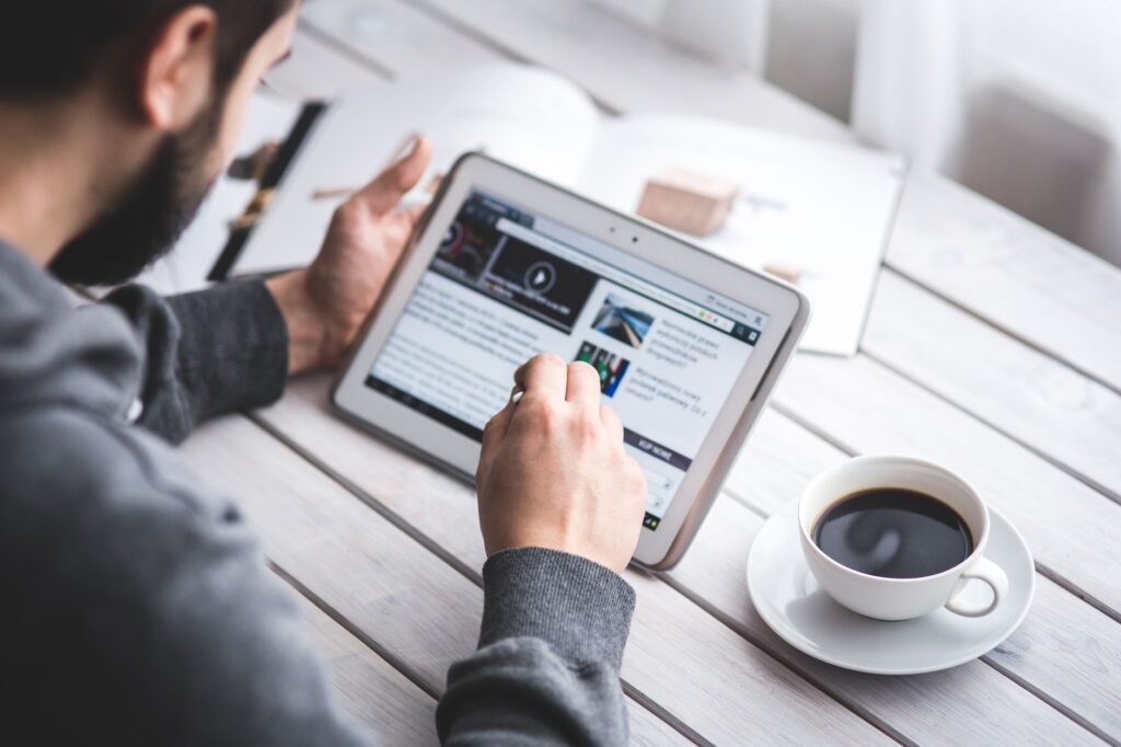 Persoană care citește știri financiare pe o tabletă, la o masă cu o cafea, dimineața